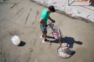 Contractor operating a walk-behind trowel machine to smooth fresh concrete