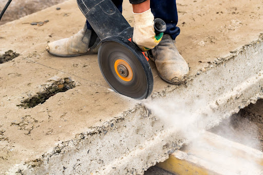  A worker uses a concrete saw rental to cut through a thick concrete slab.